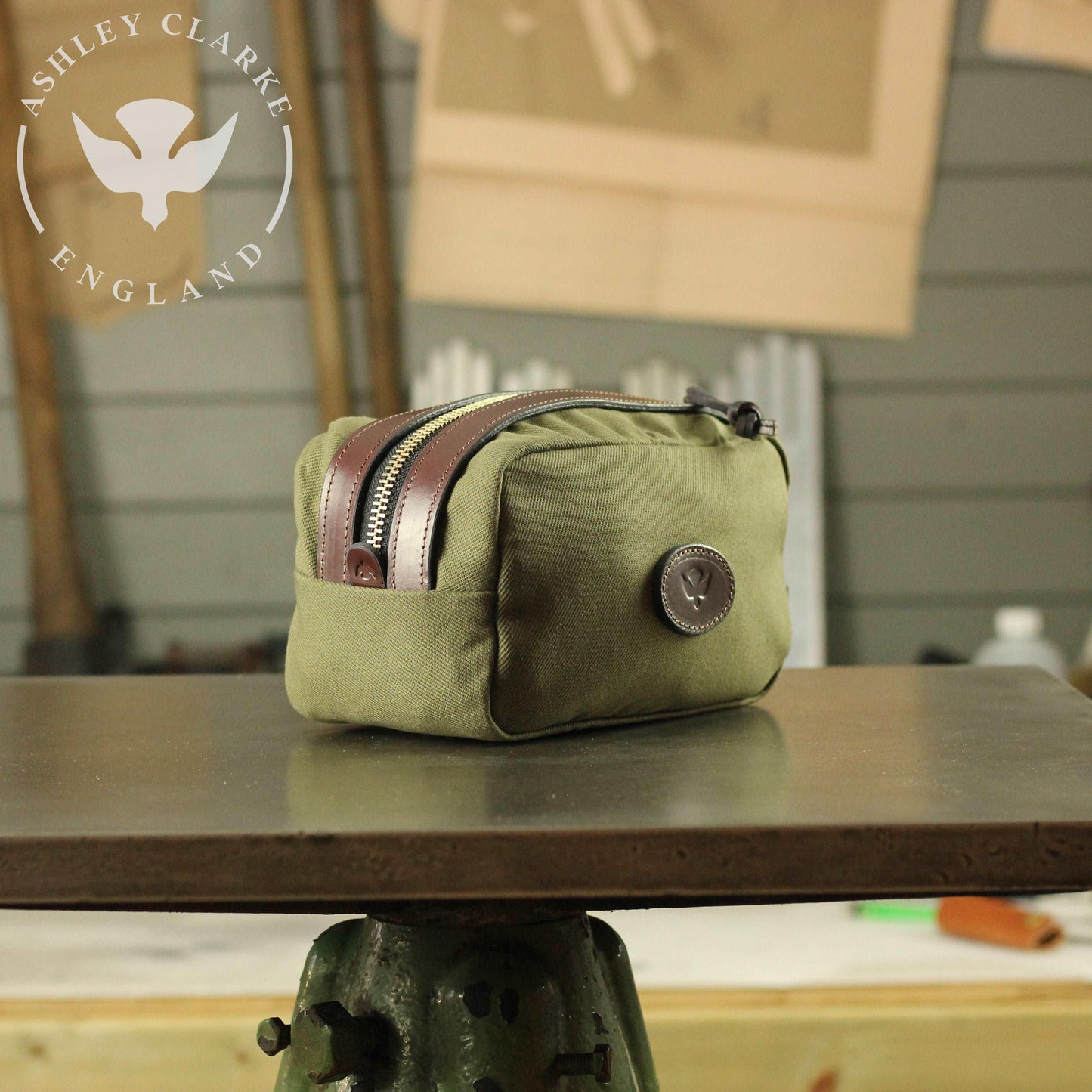 front side view of a waxed canvas wash bag by ashley clarke england on top of a table workshop 