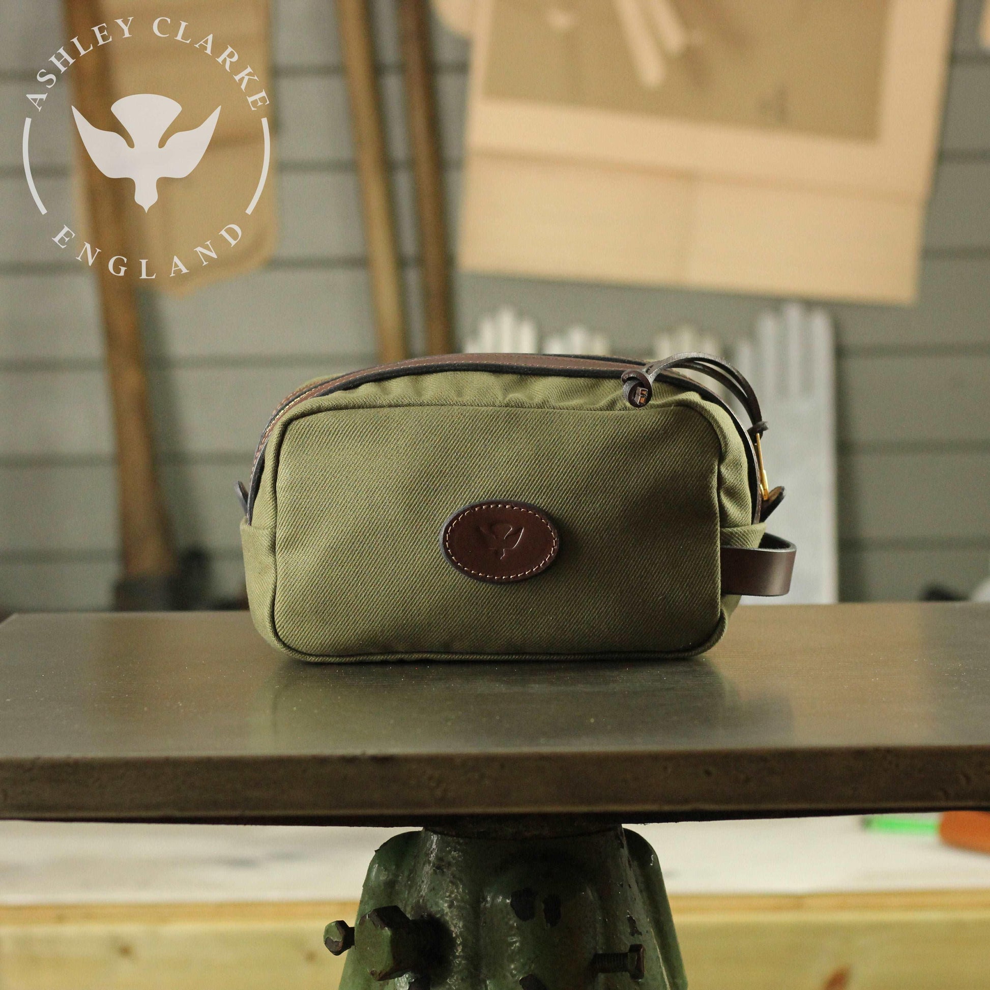 front view of a waxed canvas wash bag by ashley clarke england on top of a table workshop 