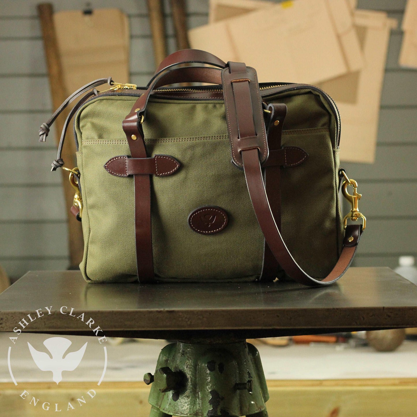 front view of a green waxed canvas briefcase laptop bag by ashley clarke on a table