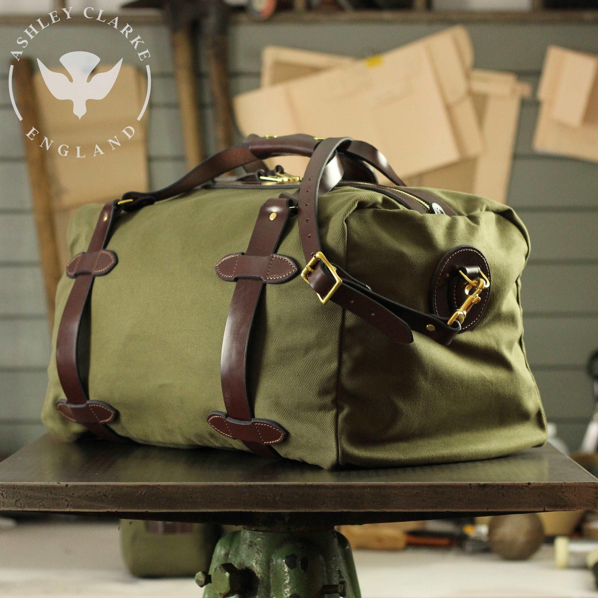 a green waxed canvas holdall bag by ashley clarke england on top of a table