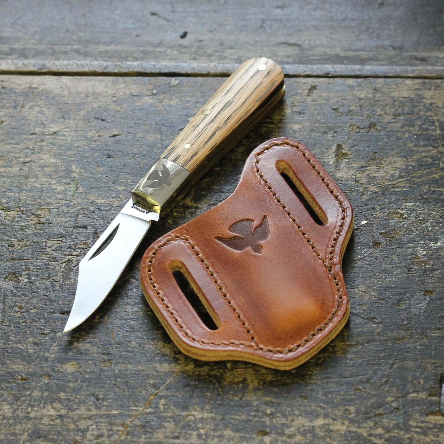 a pocket knife beside a leather holster with the ashley clarke logo stamp